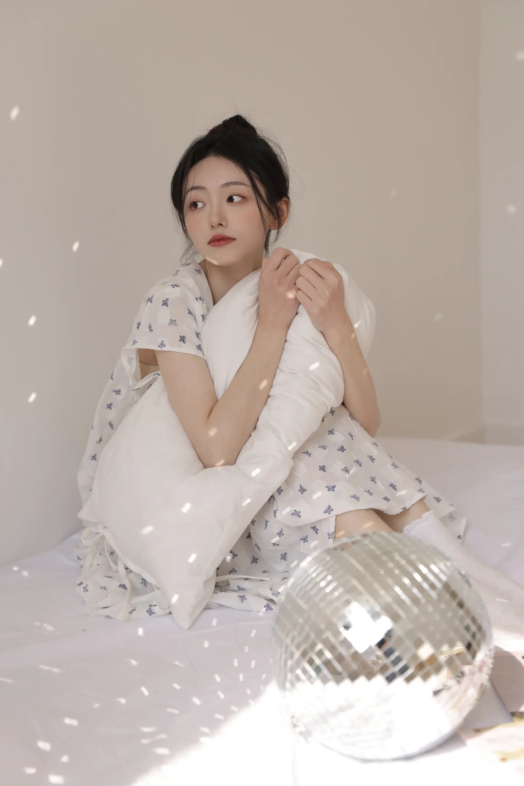 女人坐在床上，拿着枕头和迪斯科球