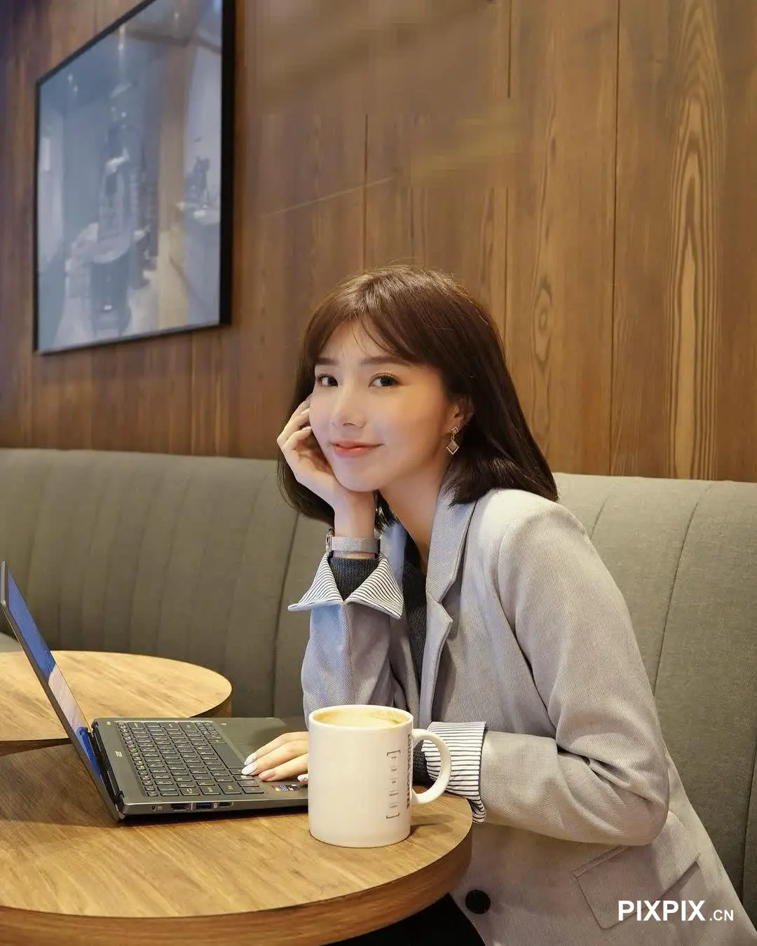 坐在桌子旁的女人拿着笔记本电脑和一杯咖啡