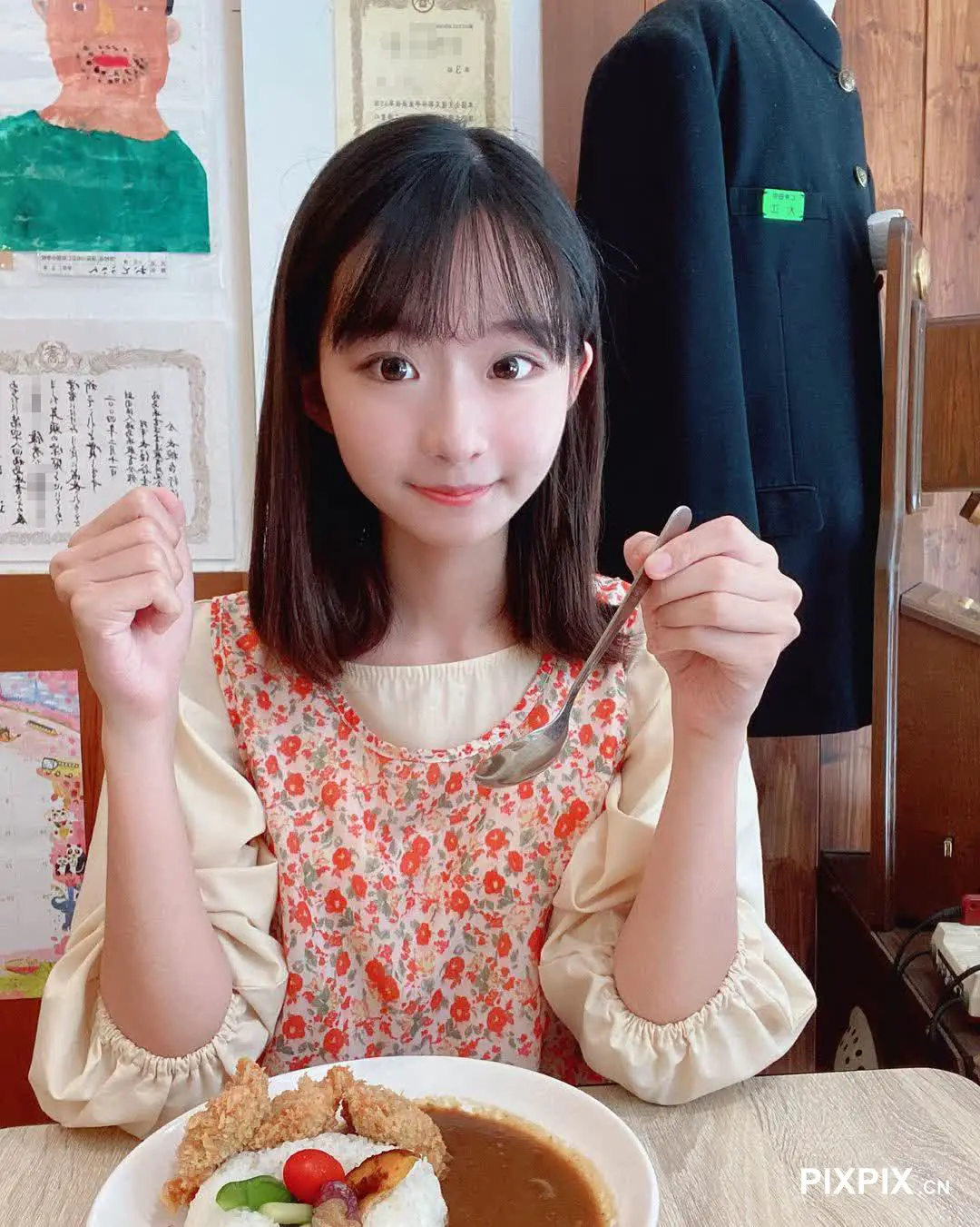 女孩坐在桌子旁，拿着一盘食物和叉子