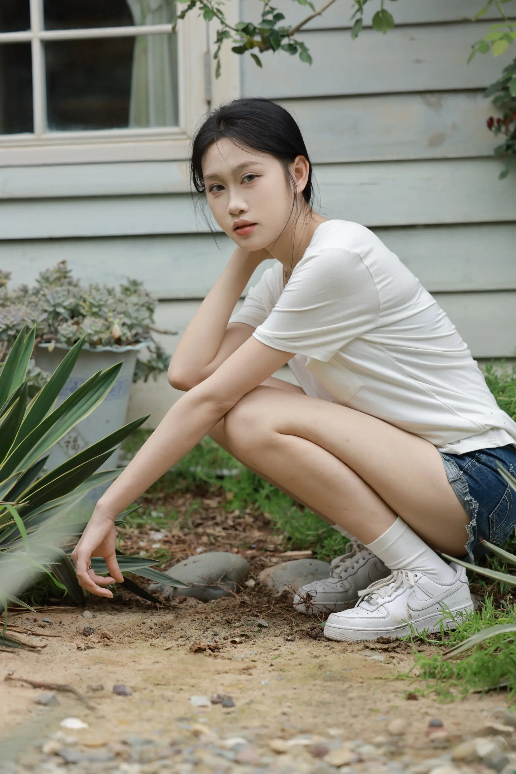 蹲在一栋有植物的房子前的女人